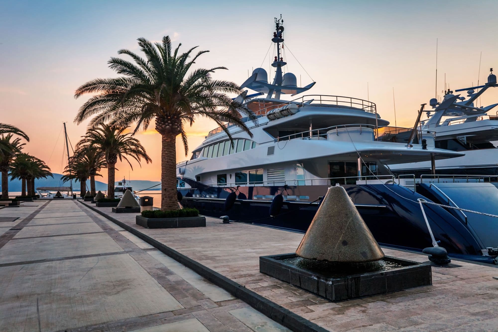 Superyachts moored along a palm-lined marina at sunset